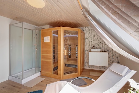 Ein Zimmer mit Duschkabine aus Glas, einer Holzsageneinrichtung, einem weißen Waschbecken und einem Liegestuhl.. Ferienhaus 'Schnettler' mit Sauna