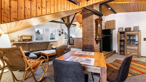A cozy living area with a wooden ceiling, a brick fireplace, a dining table with chairs, and a sofa. - Apartment 'Küstenliebe' with Shared Terrace, Shared Garden and Wi-Fi (Lehe)