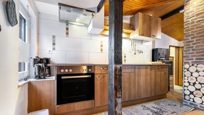 A modern kitchen with wooden cabinets, a built-in oven, and a stone wall. - Apartment 'Küstenliebe' with Shared Terrace, Shared Garden and Wi-Fi (Lehe)