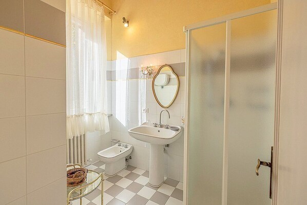 A bathroom with a bidet, a pedestal sink, a mirror, and a glass door.