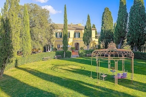 A garden with a gazebo, a building with a tiled roof, and tall trees. - Villa Farnetta Grande: A spacious and welcoming three-story villa located in the heart of the Val d'Orcia, with Free WI-FI. (Radicofani)