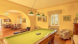 Una mesa de billar en una habitación con zona de comedor, un radiador y cuadros en la pared.