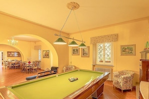 A pool table in a room with a dining area, a radiator, and framed pictures on the wall.