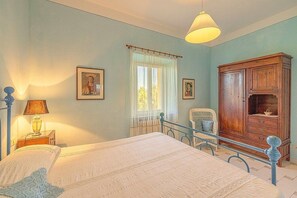 Une chambre à coucher comprenant un lit, une table de chevet, une lampe, une chaise, une armoire et deux tableaux encadrés accrochés au mur.