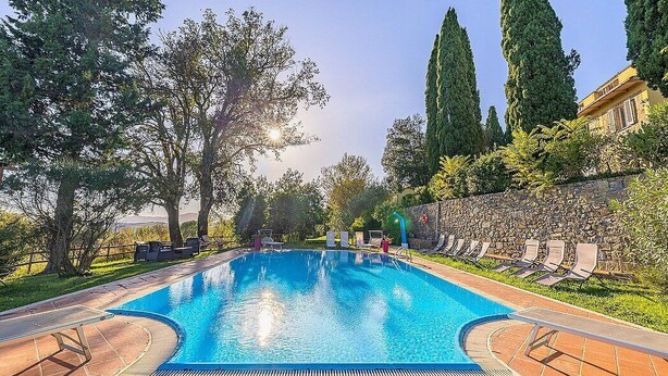 Una piscina con sillas de descanso, árboles y un muro de piedra.