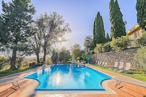 Une piscine entourée de chaises longues, d’arbres et d’un mur en pierre.