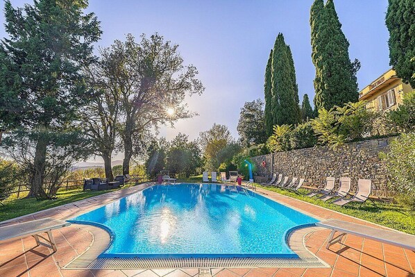 A swimming pool with lounge chairs, trees, and a stone wall.
