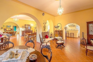 A spacious interior with a dining area, multiple seating arrangements, and a kitchen visible through an archway.