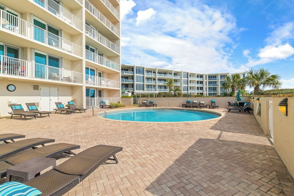 Uma área de piscina de hotel com espreguiçadeiras, piscina e um edifício com várias andares e varandas.