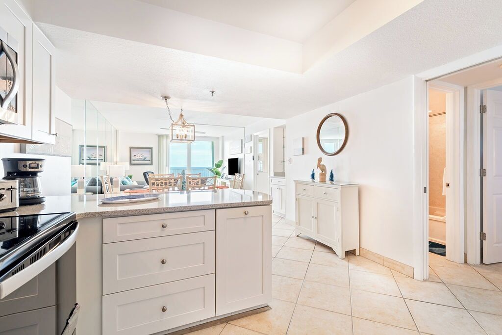 A modern kitchen with white cabinetry, a large island, and a view to the living area.