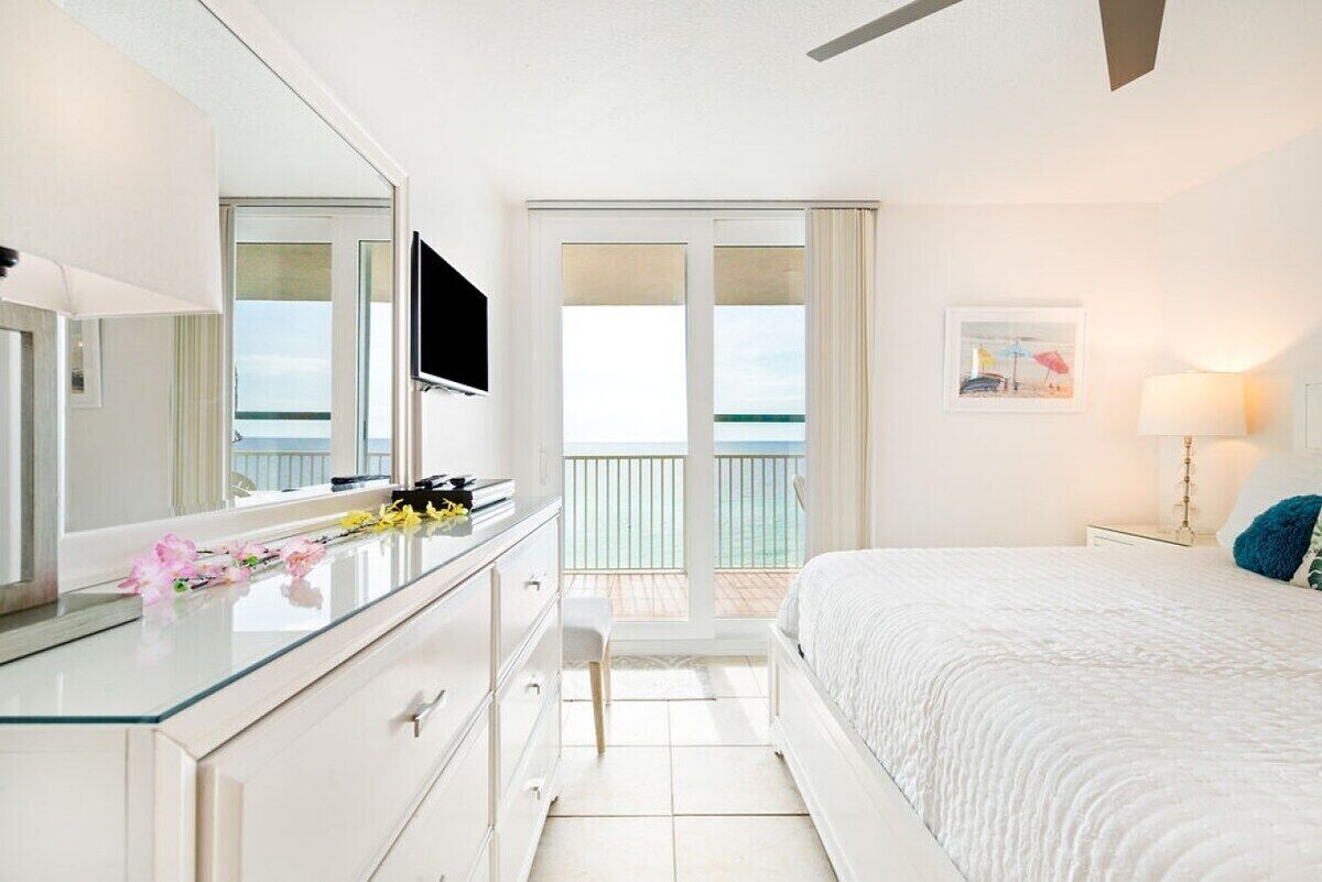 Une chambre d’hôtel avec un lit, une commode, un miroir, une télévision et un balcon donnant sur l’océan.