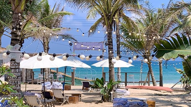 A beachside café with outdoor seating, palm trees, and string lights. - harbor Surf Hotel (Wanning)