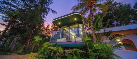 Una estructura moderna, con paredes de vidrio y techo curvo, rodeada de exuberante vegetación tropical.