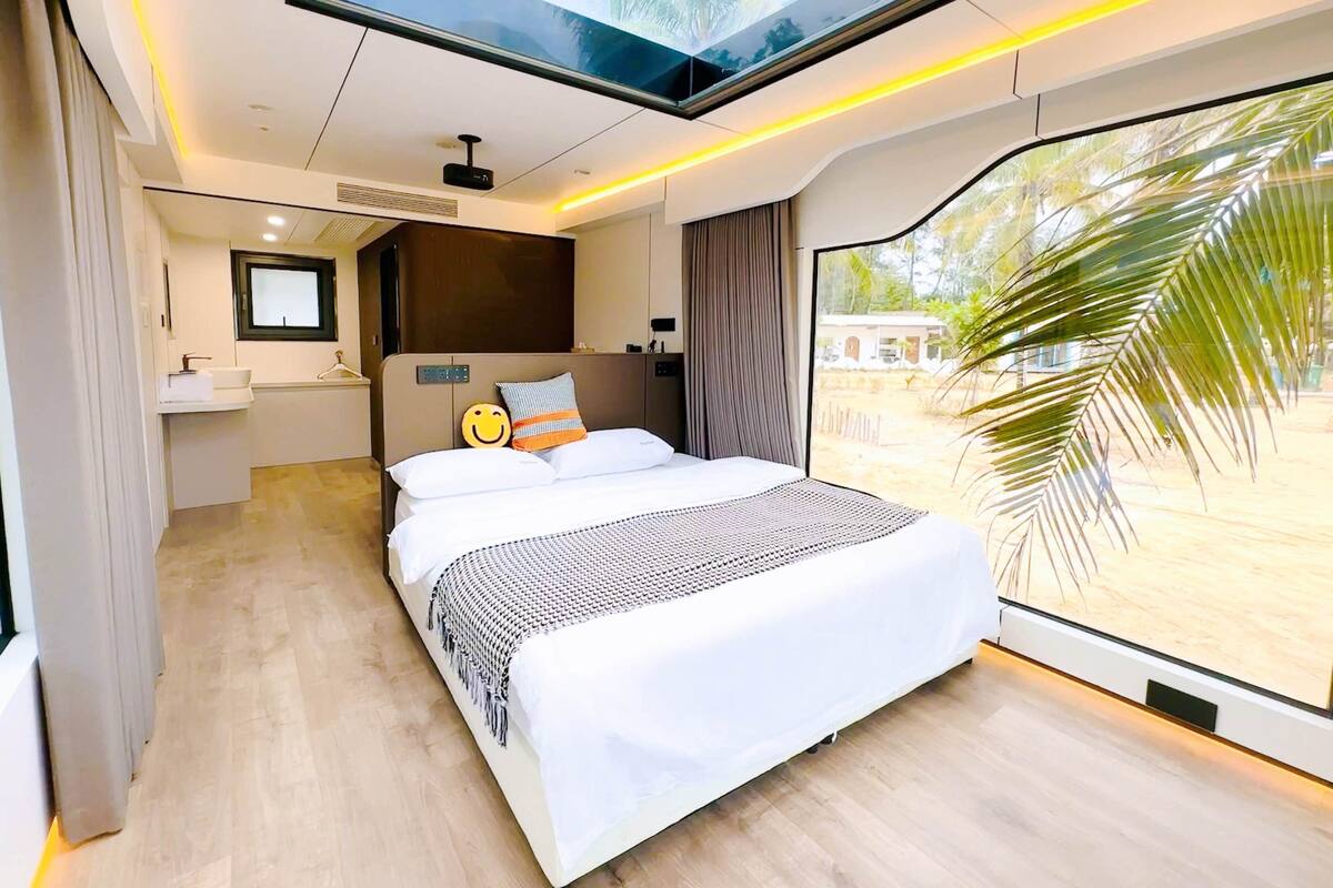 A modern hotel room with a skylight, a large bed, a bathroom, and a view of the outdoors.