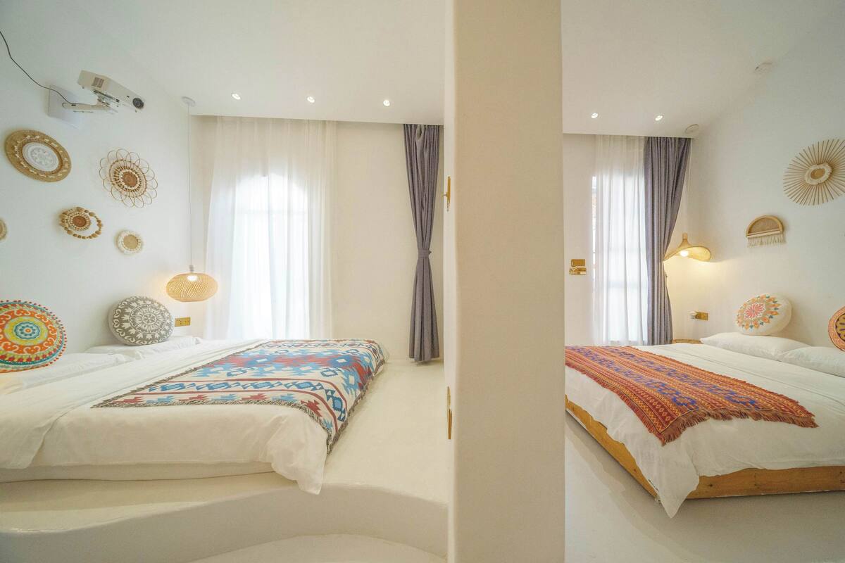 A room with two beds, a projector, and decorative wall hangings.