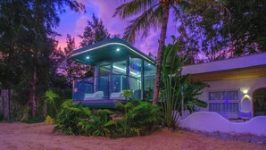 A modern glass house with a curved roof, surrounded by tropical plants and palm trees. - harbor Surf Hotel (Wanning)