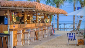 A beachside bar with a thatched roof, wooden bar counter, and multiple stools. - harbor Surf Hotel (Wanning)