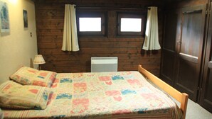 Et soveværelse med sengegavl i træ, en seng med farverigt quilt, en sengebordlampe og et vindue med gardiner.