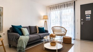 A modern living room with a sofa, a wicker chair, a glass coffee table, and a lamp.