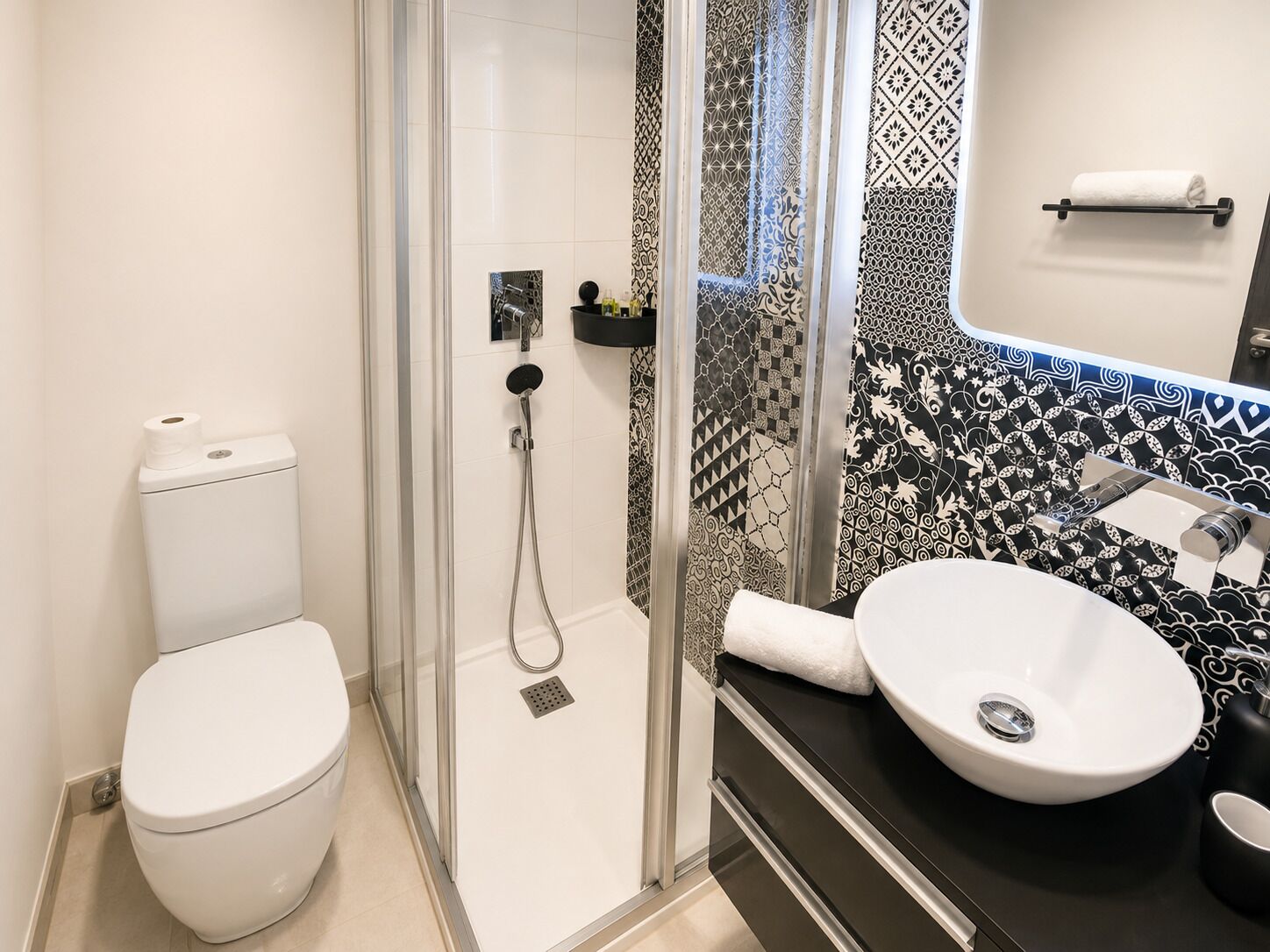Un baño moderno con inodoro, ducha con cerramiento de vidrio y lavamanos con encimera negra.