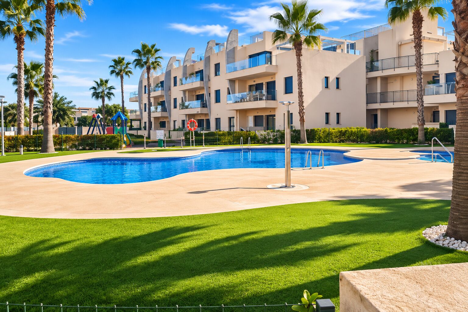 A swimming pool with a curved edge, surrounded by palm trees and a well-maintained lawn.