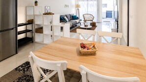 A modern kitchen with a dining area, white furniture, and a view to the living room.