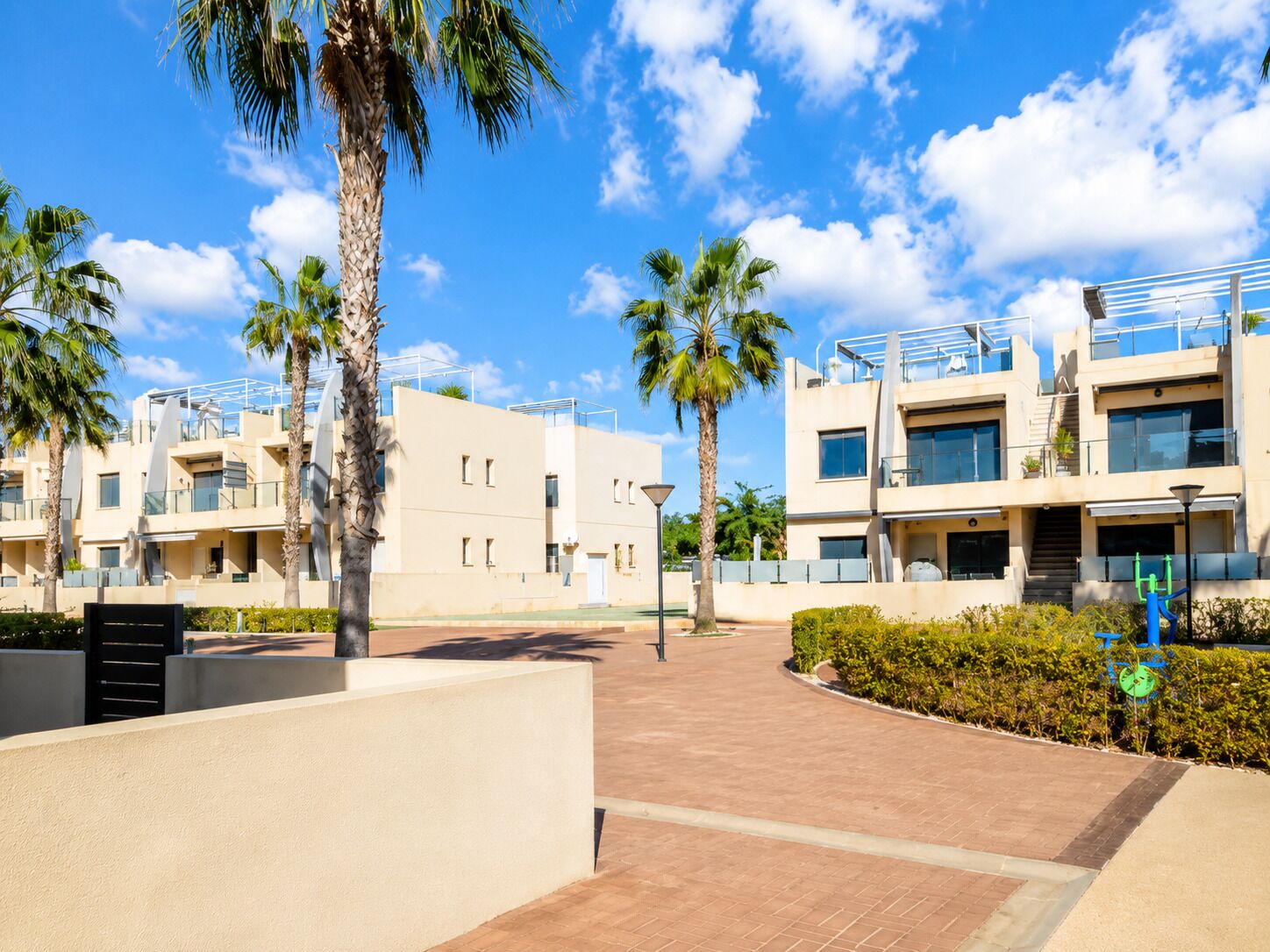 A modern building with multiple balconies, palm trees, and a clear blue sky.