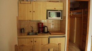 Eine kompakte Küche mit Holzausstattung, einer Mikrowelle, einer Kaffeemaschine und einem Waschbecken.