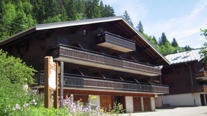 Eine zweigeschossige Holzchalet mit Balkonen, umgeben von üppiger Vegetation und einem bewaldeten Hintergrund.