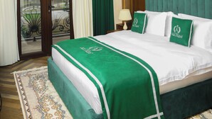 Habitación de hotel con una cama grande, una araña, un cabecero tapizado en verde y vistas a través de un ventanal.