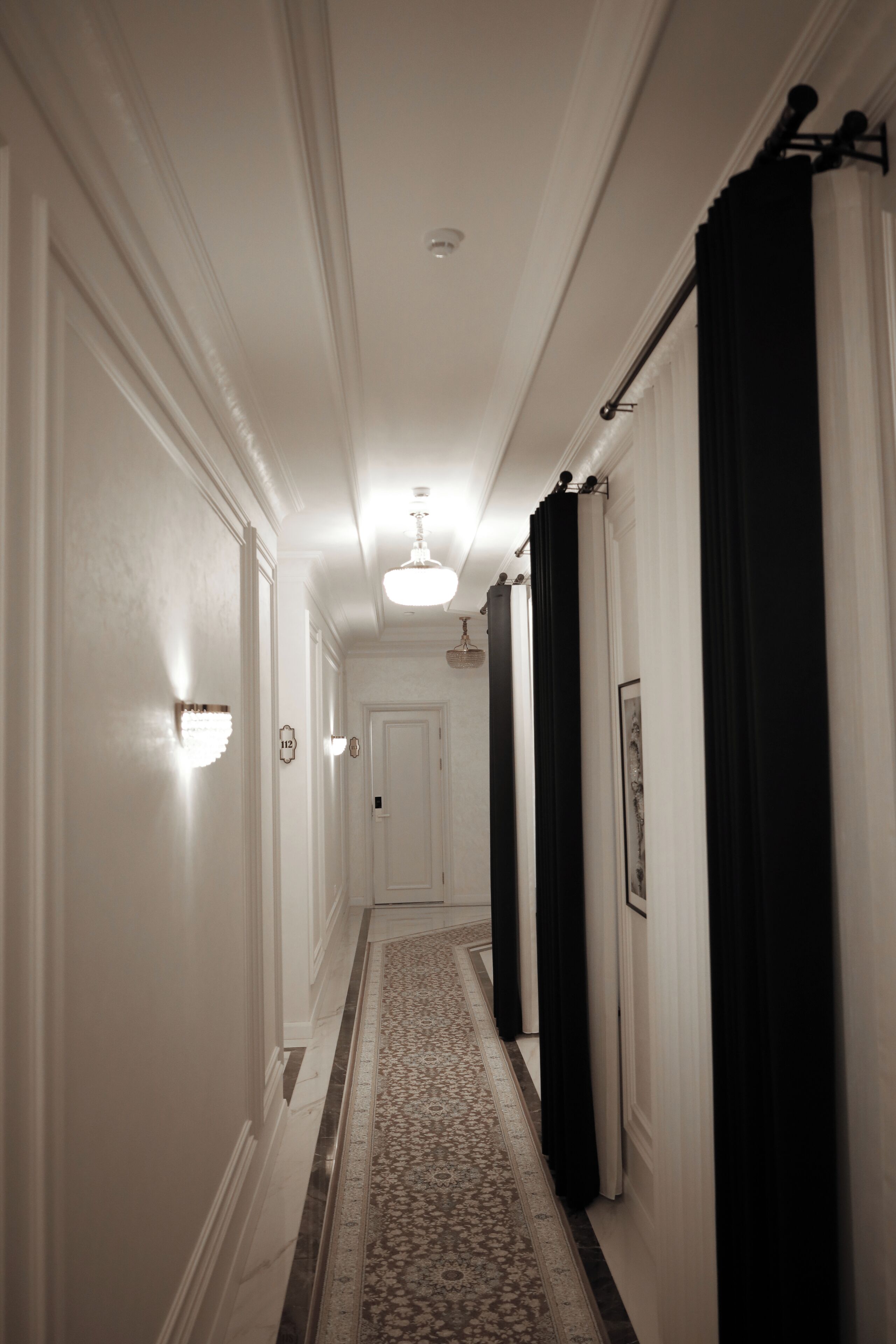 A hallway with white walls, a patterned carpet, and black curtains.