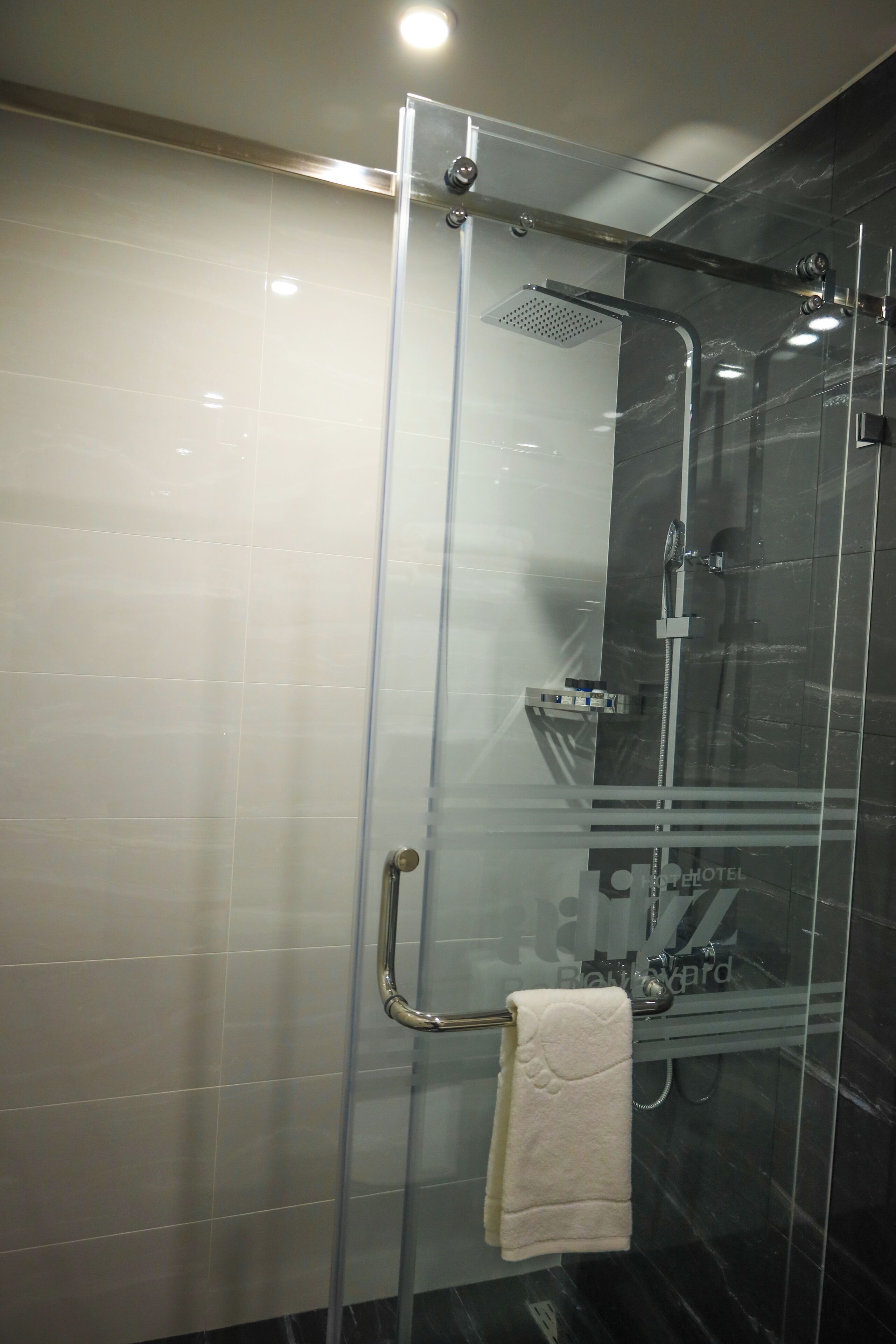 A glass-enclosed shower with a handheld showerhead and a towel rack with a towel.