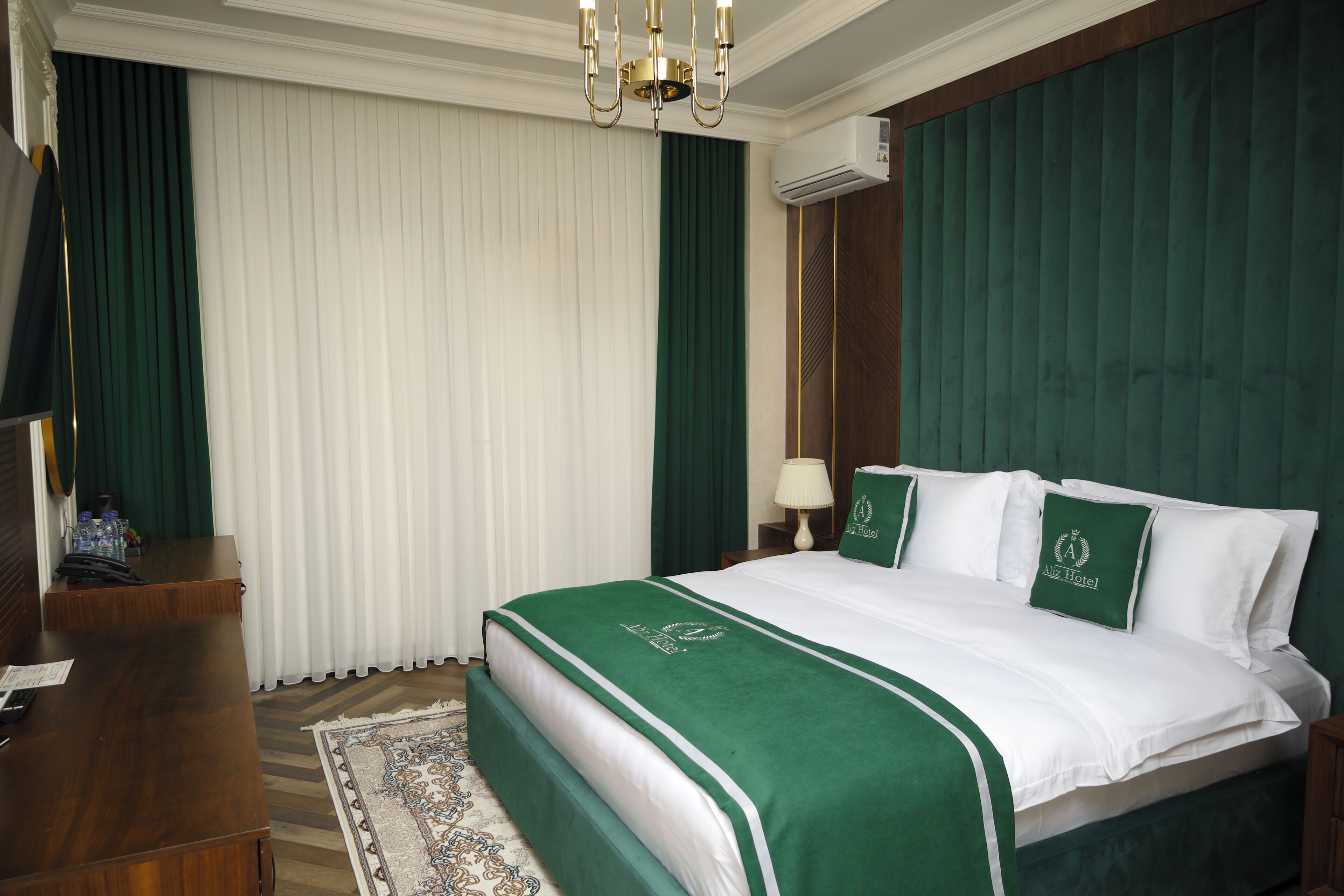 Una camera d'albergo con un letto grande, biancheria verde e bianca, un comodino in legno con una lampada e una tenda verde.