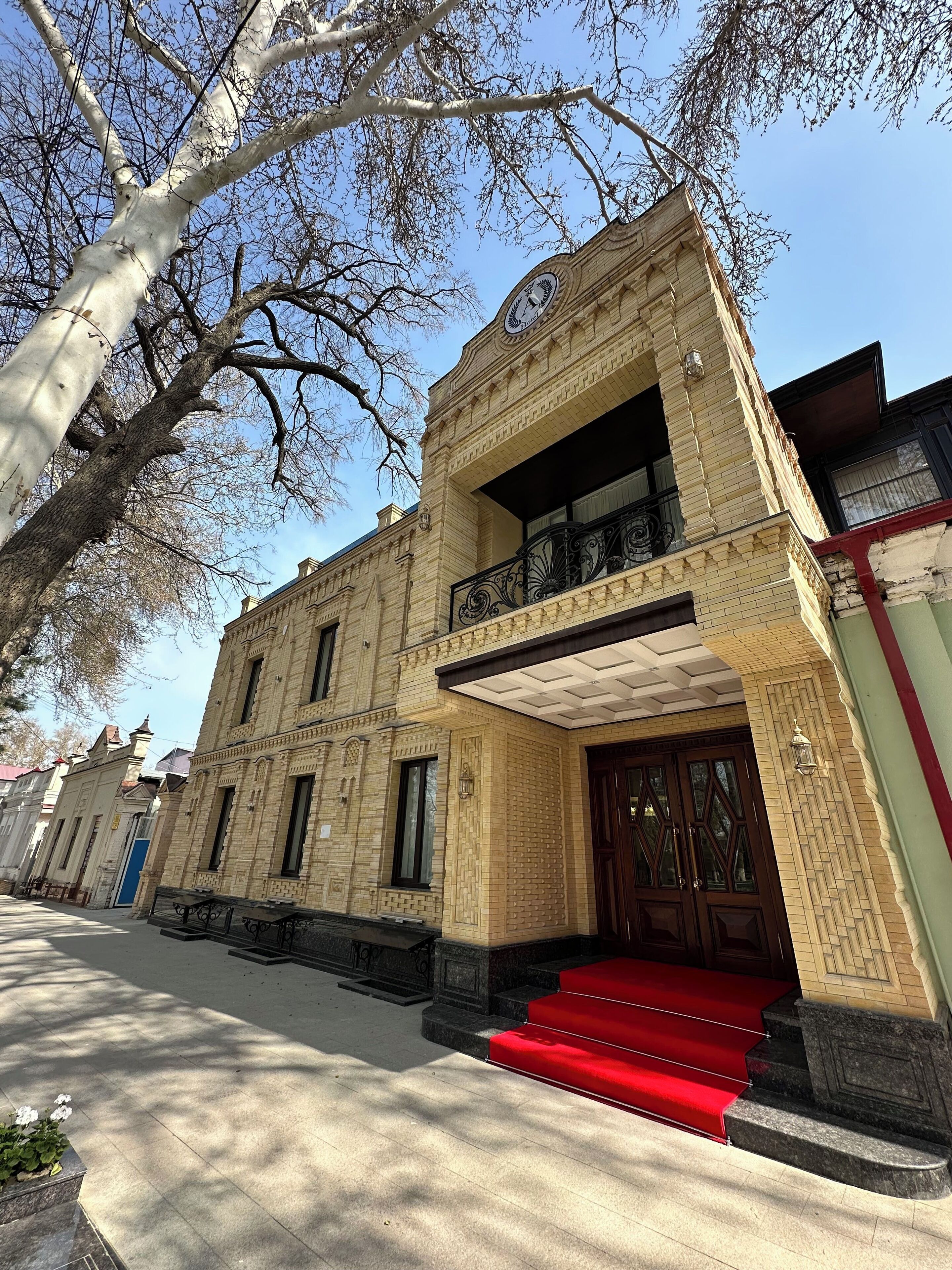 A historic building with a prominent entrance, a balcony, and a red carpet leading to the main door.
