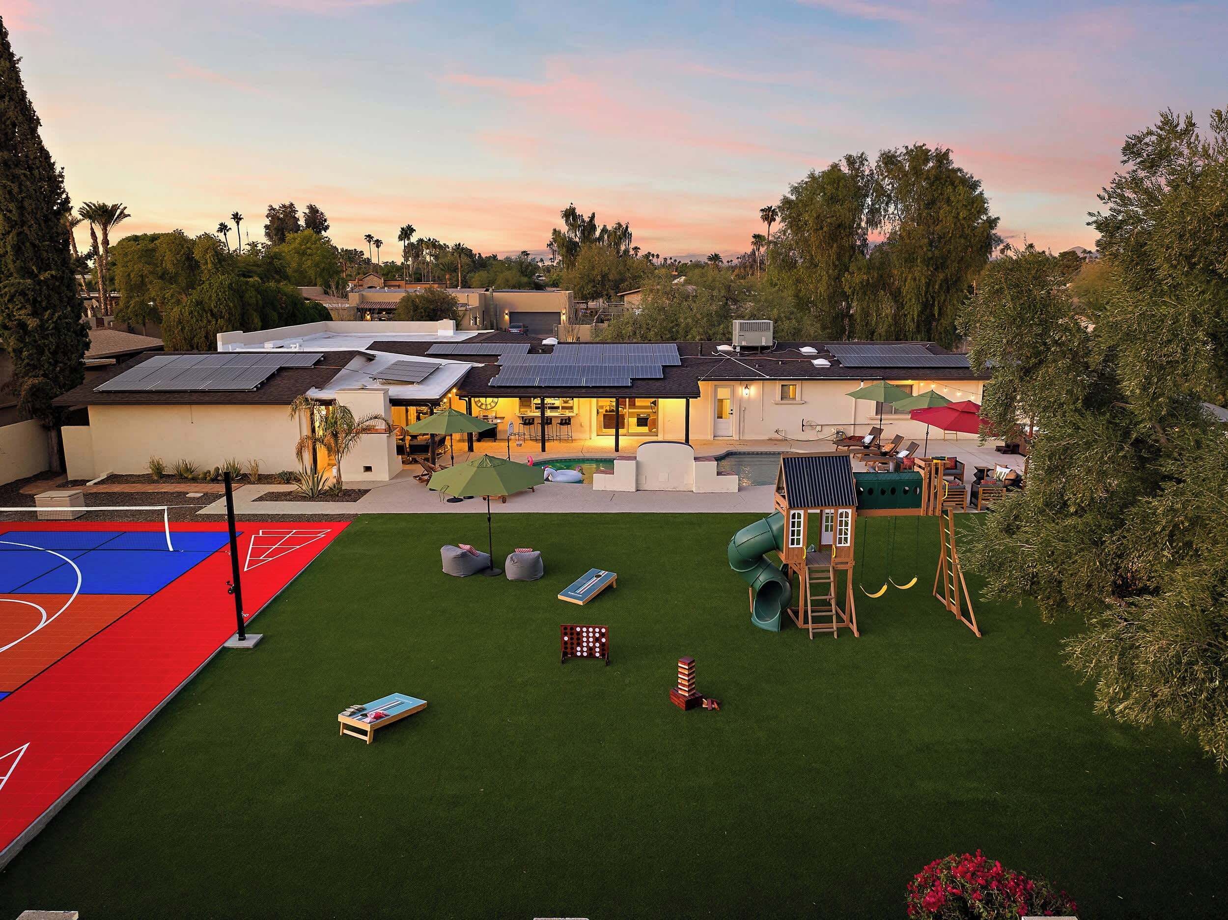 Een woonhuis met een zwembad, terras, basketbalveld en zonnepanelen.
