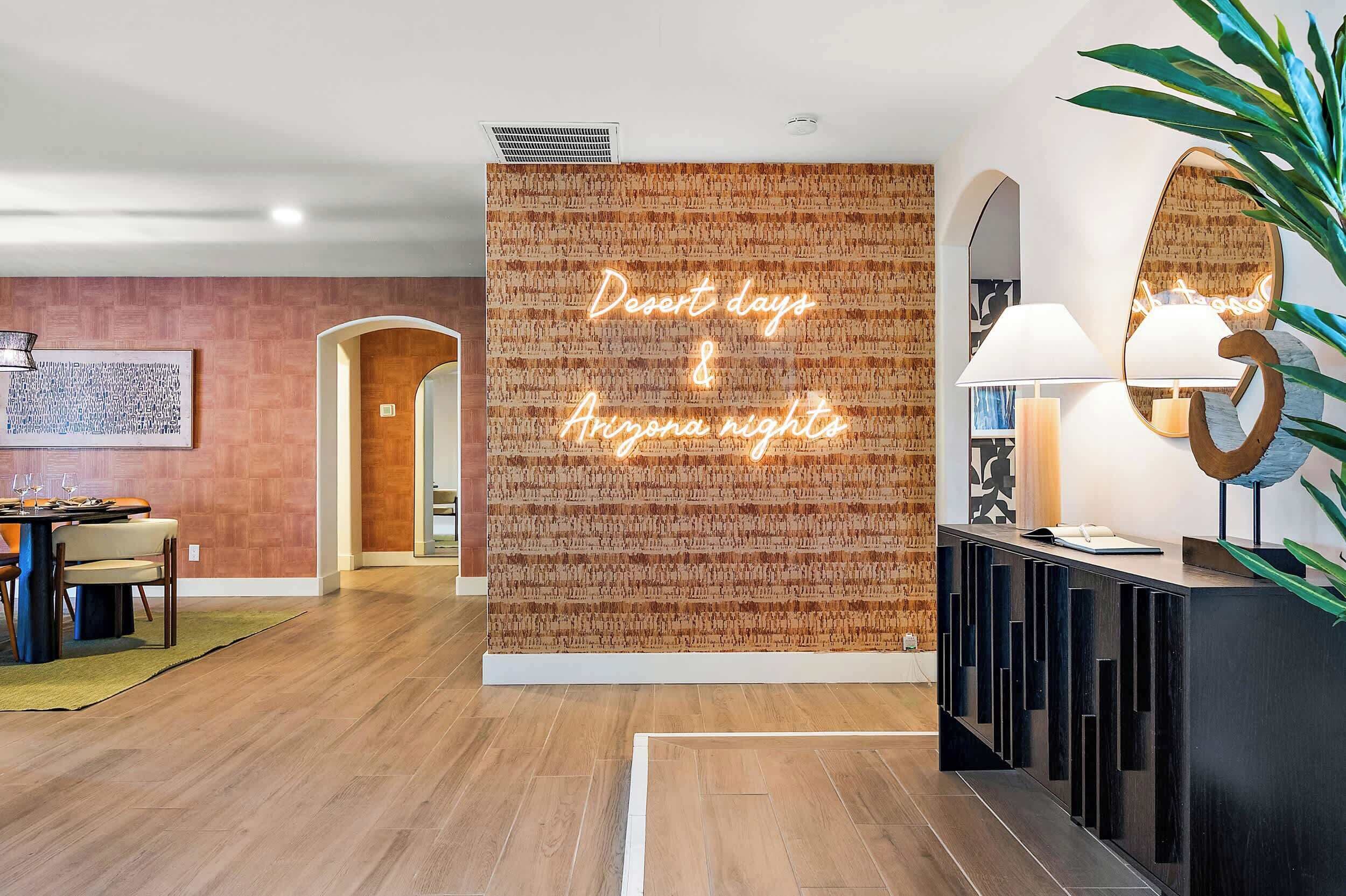 A modern hotel lobby with a wooden wall, a neon sign, a reception desk, and a dining area.