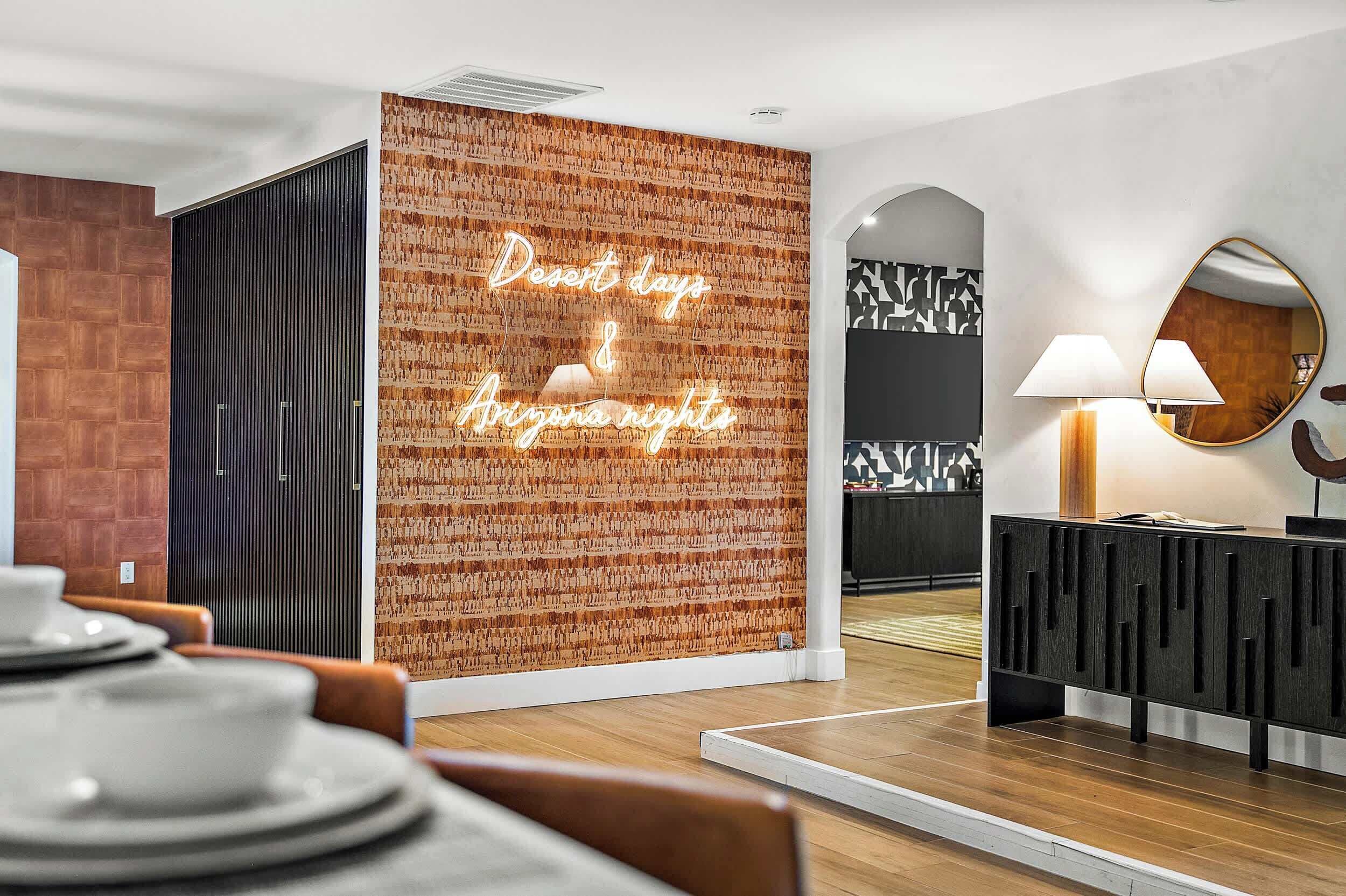 A modern interior with a neon sign reading "Desert days & Arizona nights," a wooden wall, a black cabinet, and a round mirror.