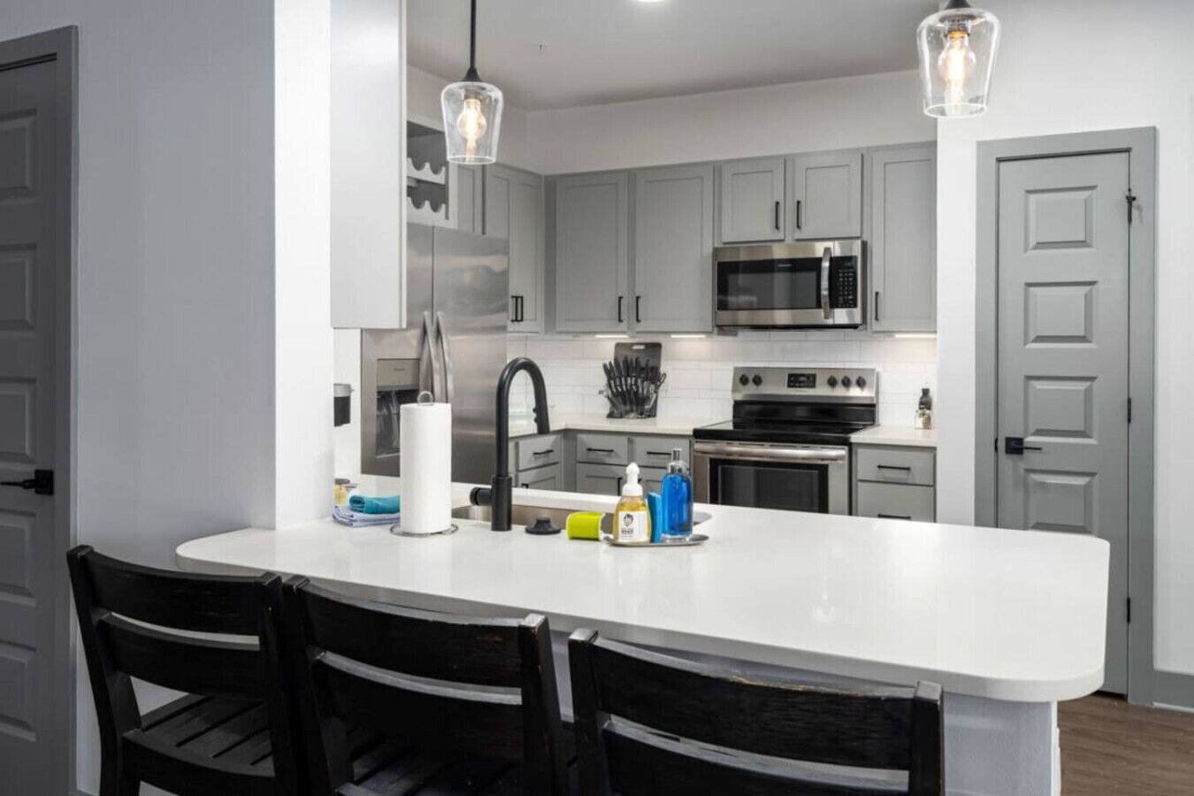 A modern kitchen with a central island, stainless steel appliances, and black chairs.
