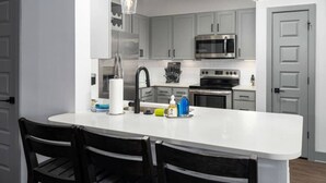 A modern kitchen with a central island, stainless steel appliances, and black chairs.