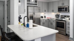 A modern kitchen with grey cabinets, stainless steel appliances, and pendant lighting.