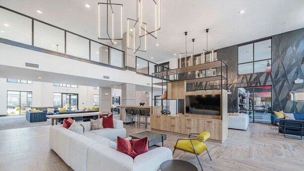 A spacious living area with a high ceiling, modern furniture, and a kitchen area visible in the background.