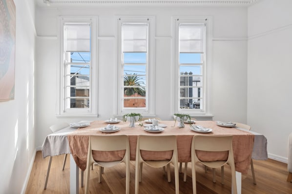 A dining room with a table set for four, large windows, and a view of buildings and palm trees outside.