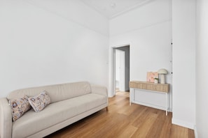 A minimalist living room with a beige sofa, patterned cushions, a wooden console table with a lamp, and a framed picture.