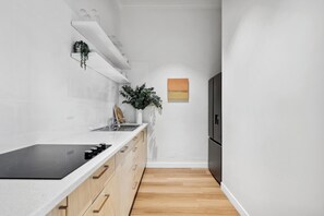 A modern kitchen with white cabinetry, a black induction cooktop, and a wooden floor.