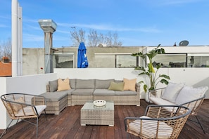 A rooftop patio with a sectional sofa, wicker chairs, and a small table.