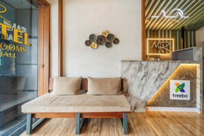 A reception desk with a marble counter, a bed with wooden headboard and beige cushions, and a wall-mounted decorative item. - Treebo MR Motel, 10 Mins To Airport (Iritty)