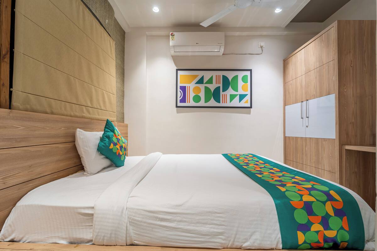 A neatly made bed with a colorful blanket, a pillow, and a wall-mounted air conditioner.