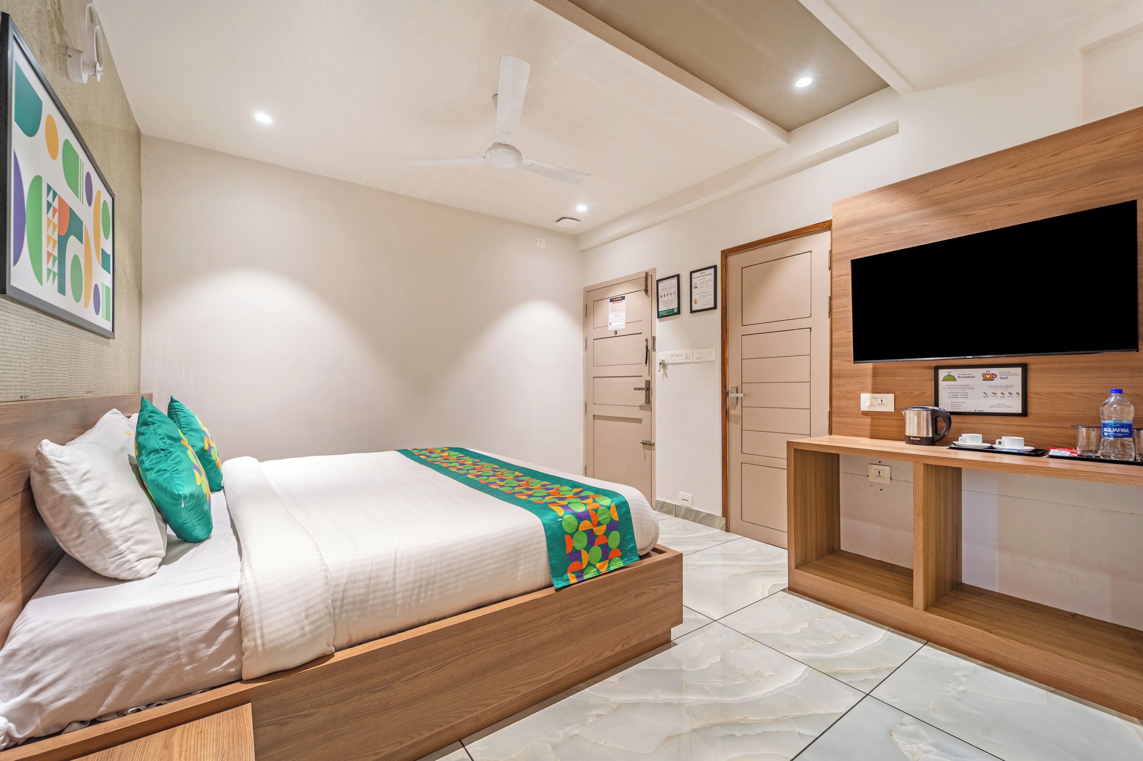 A modern bedroom with a bed, a desk, a TV, and a ceiling fan.