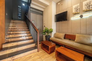 A staircase with wooden steps and a handrail, a sofa with cushions, a coffee table, a potted plant, and a flat-screen TV mounted on the wall. - Treebo MR Motel, 10 Mins To Airport (Iritty)