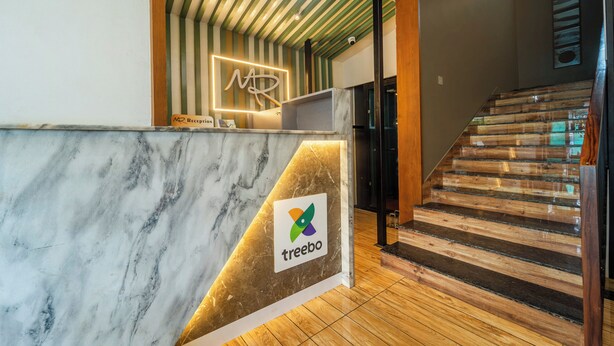 A reception desk with a marble top and a logo, a wooden staircase, and a striped ceiling. - Treebo MR Motel, 10 Mins To Airport (Iritty)